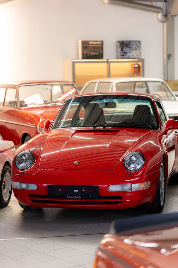 Ein roter Porsche steht neben anderen Autos in einer Garage.