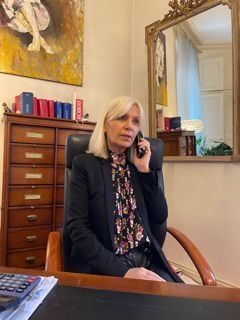 Femme en veste noire, au téléphone, assise à son bureau.