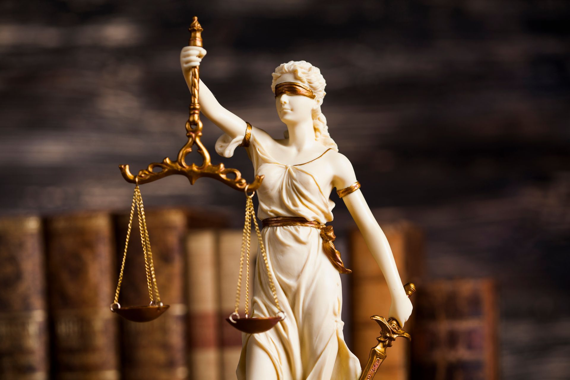 Statue de la Justice avec balance et bandeau sur les yeux, livres en arrière-plan.