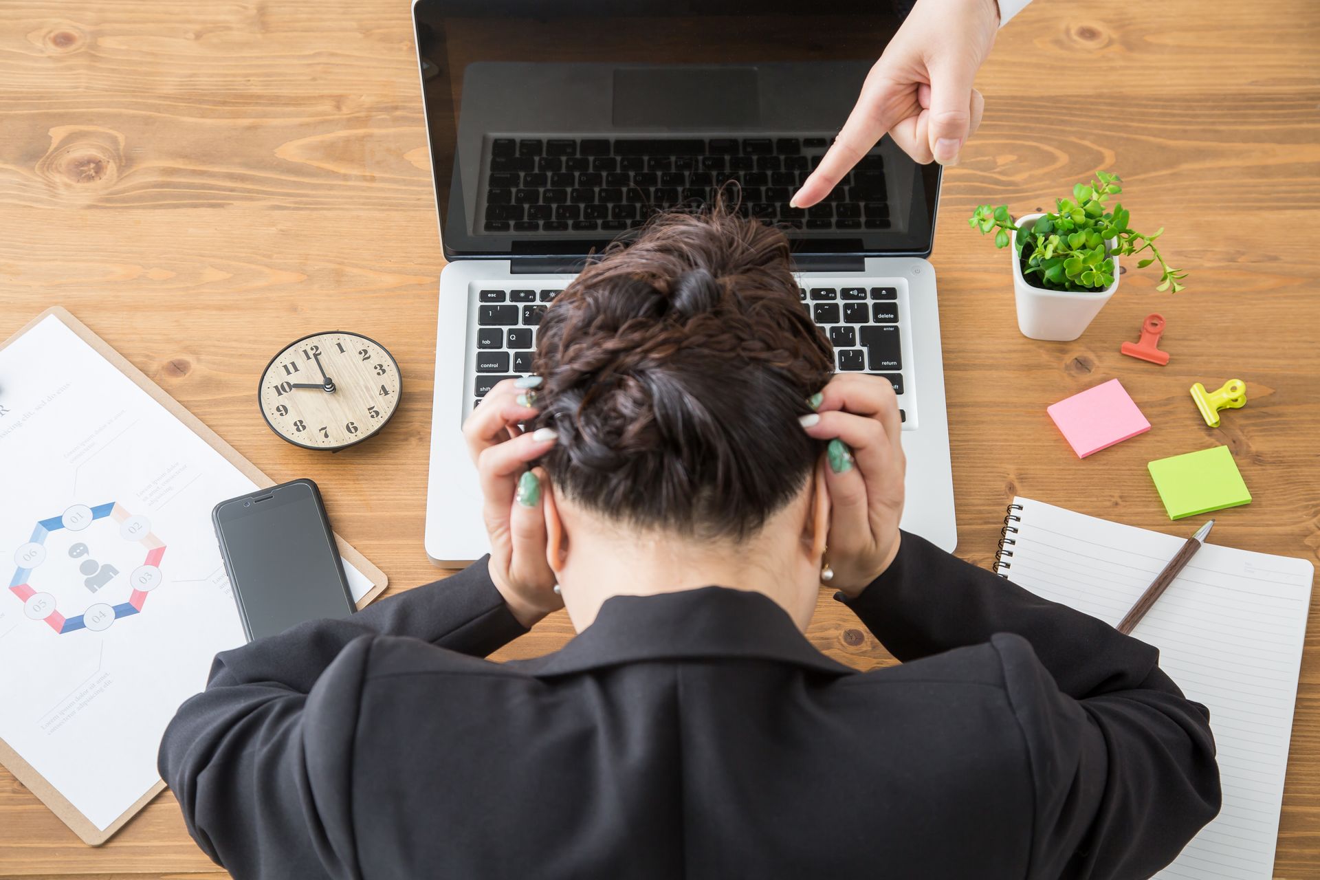 Une femme stressée, assise à son bureau, la tête entre les mains, devant l'écran de son ordinateur portable.