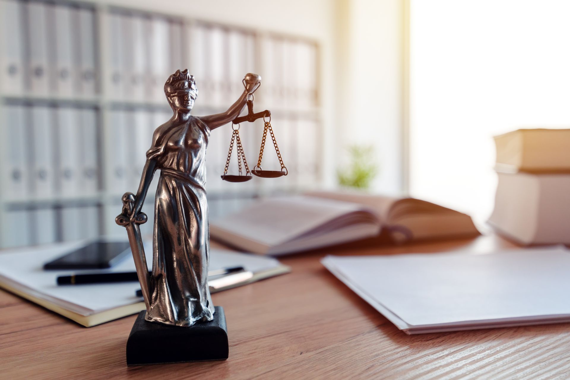 Statue de la Justice sur un bureau avec une balance, une épée et des documents, dans un décor de bureau.