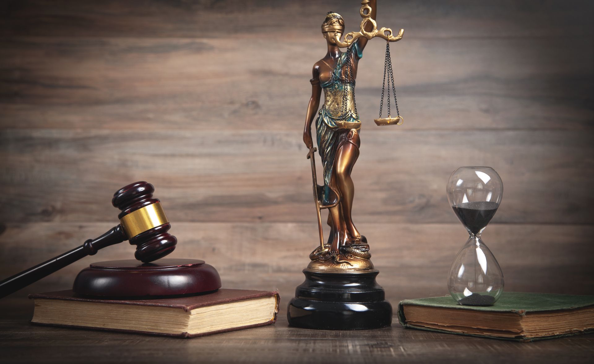 Marteau, statue de la Justice et sablier sur des livres, le tout sur fond de bois.