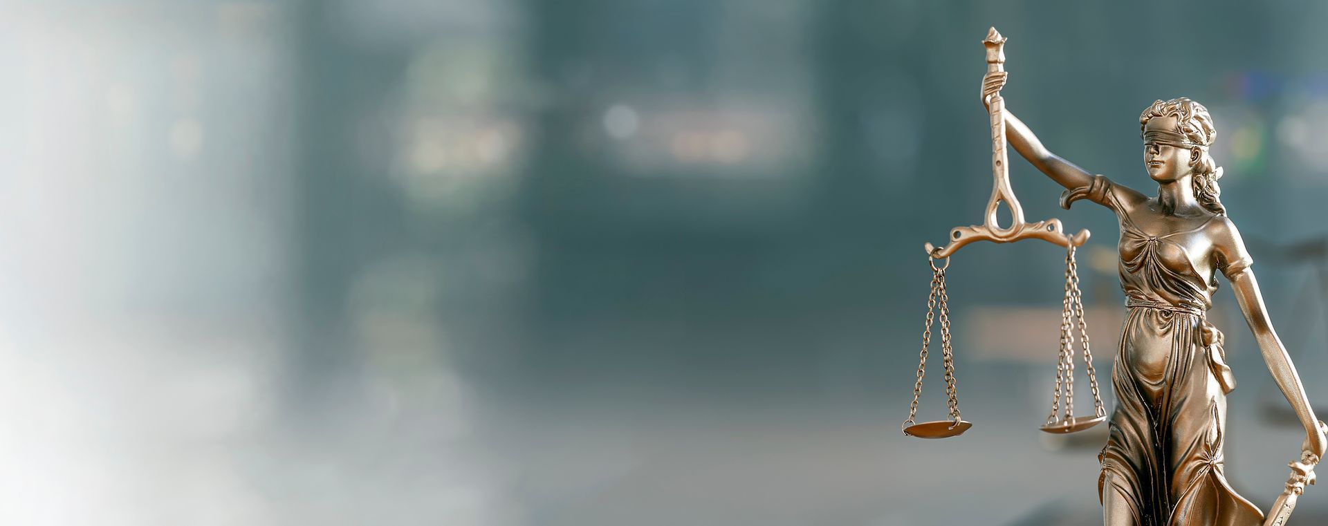 Statue de la Justice tenant une balance, sur un fond flou.