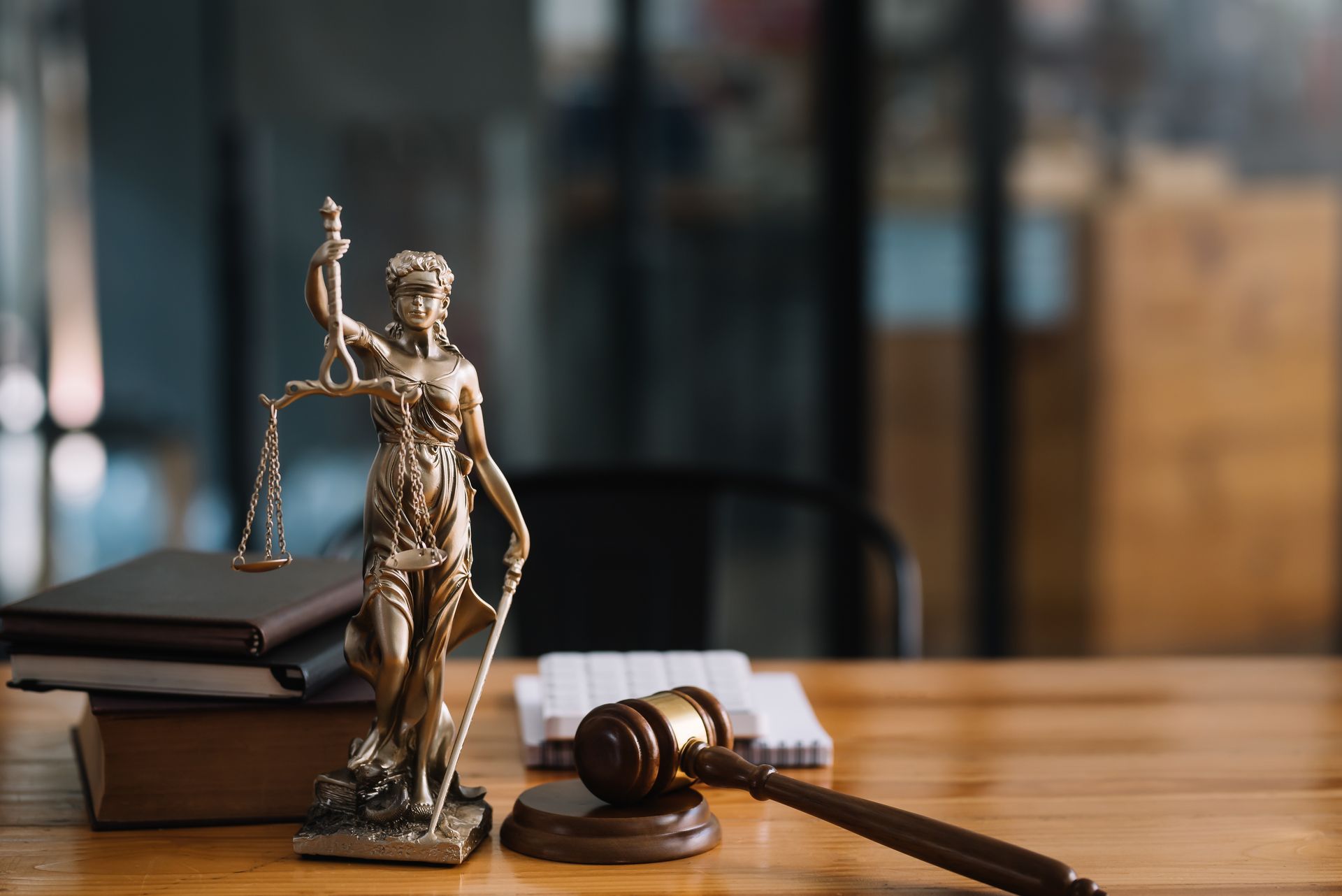 Statue de la Justice avec une balance et un maillet sur un bureau en bois, avec des livres en arrière-plan.