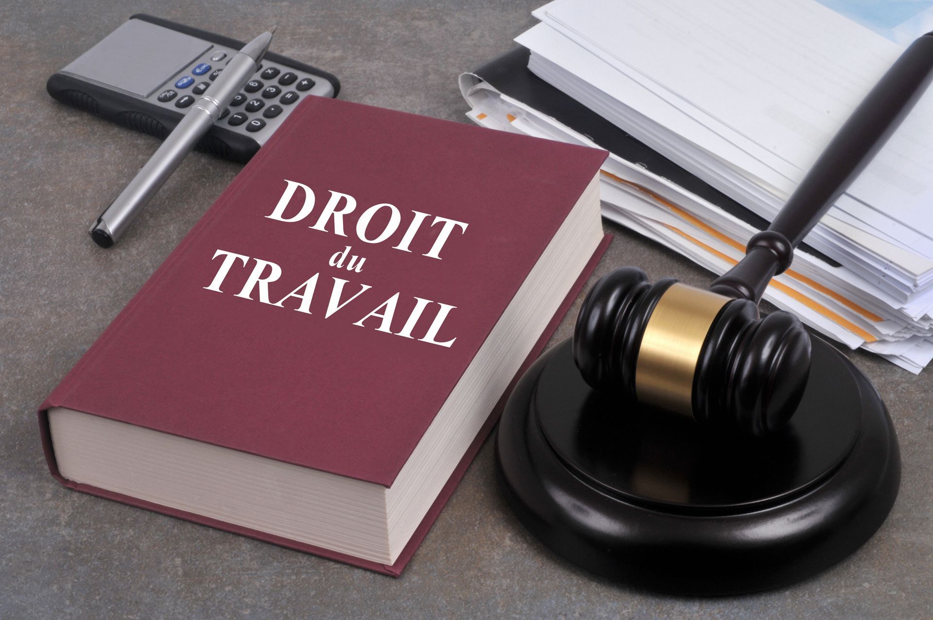Un livre intitulé Droit du Travail avec un maillet, un bloc-notes, une calculatrice et un stylo sur un bureau.