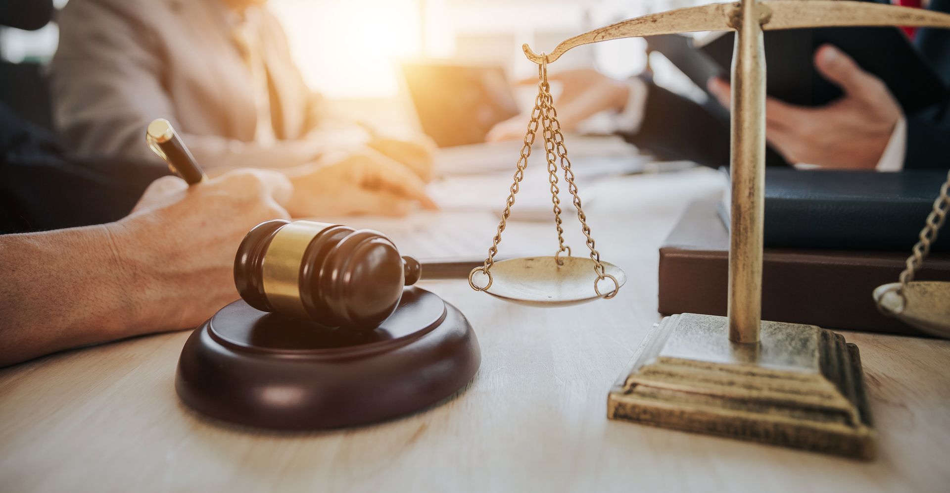 Un maillet et une balance de la justice sur une table, avec des personnes en arrière-plan.