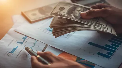 Una persona sostiene una pila de dinero y escribe en un trozo de papel.