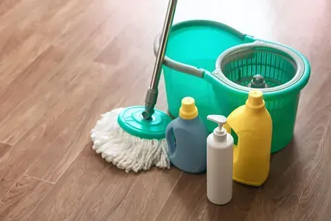 Un trapeador, un balde y botellas de productos de limpieza sobre un piso de madera.