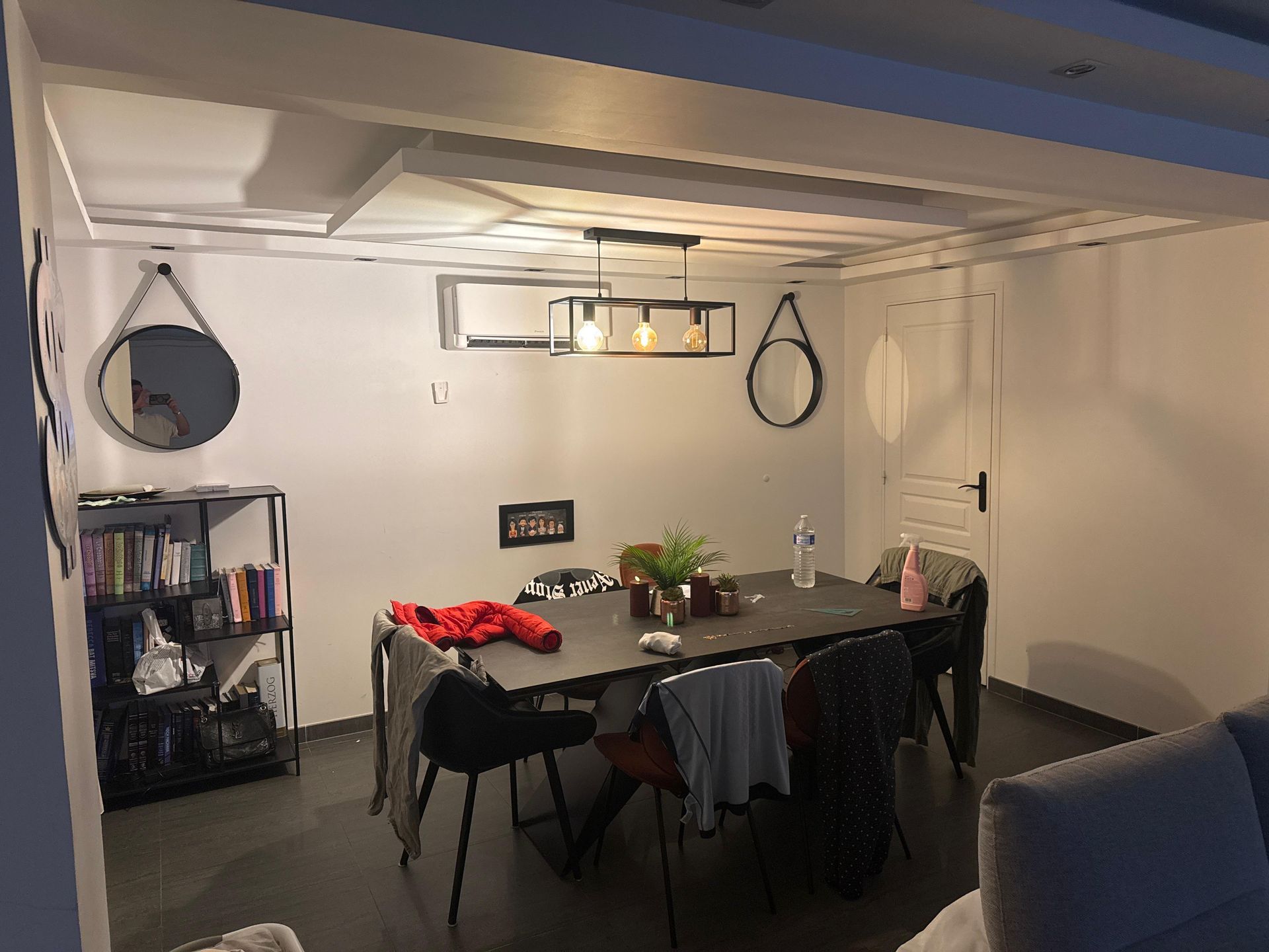 Coin repas au sous-sol avec une table, des chaises, des étagères et des sacs suspendus sous un plafond bas