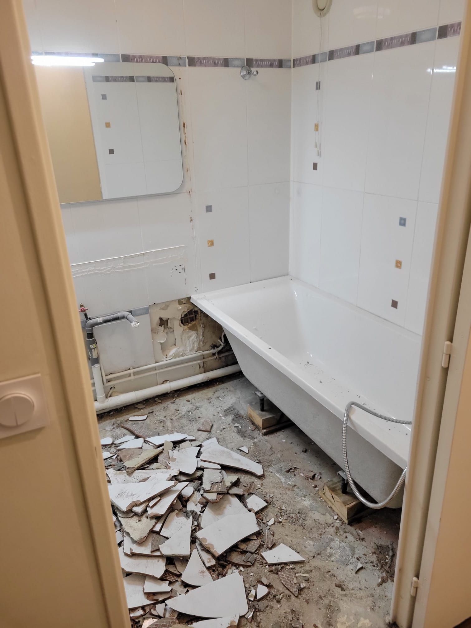 Salle de bain endommagée avec des carreaux cassés éparpillés sur le sol et une baignoire contre le mur
