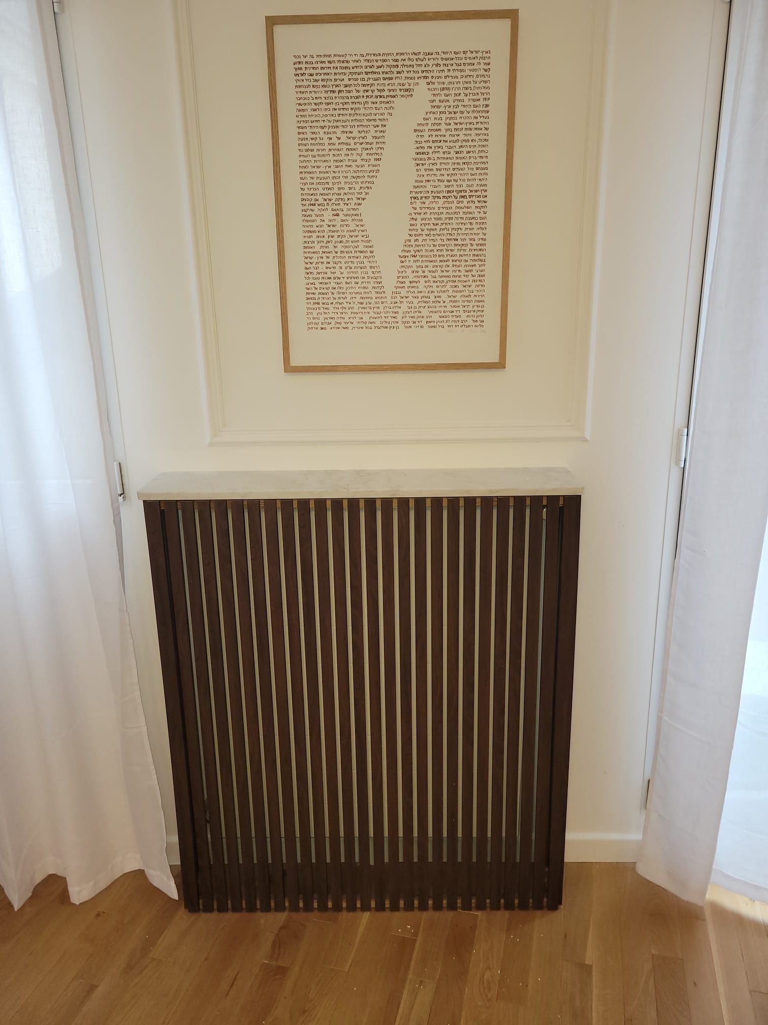 Calligraphie encadrée au-dessus d'un cache-radiateur en bois foncé dans un couloir blanc