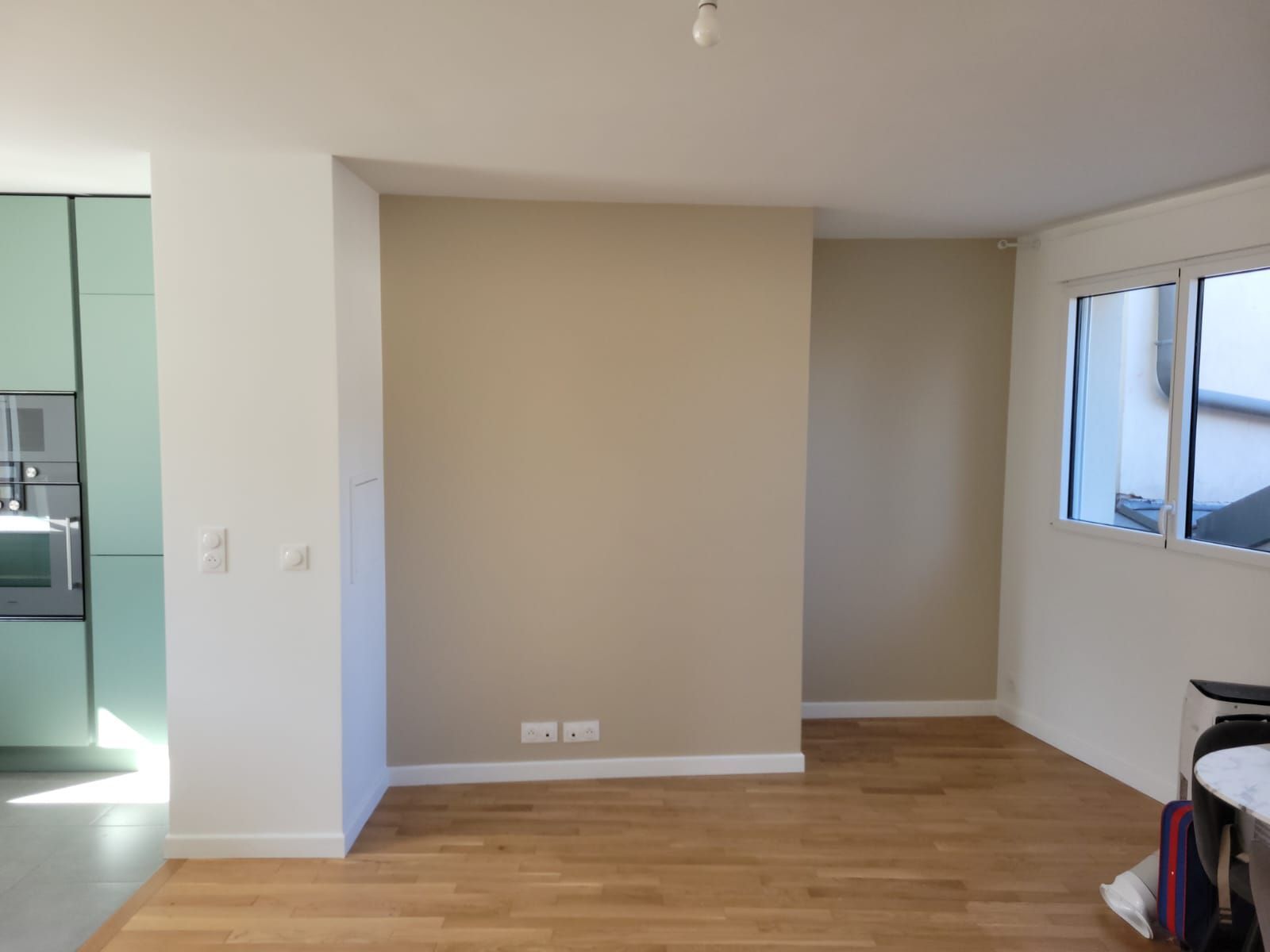 Pièce vide non meublée avec murs beiges, parquet et fenêtres sur la droite.