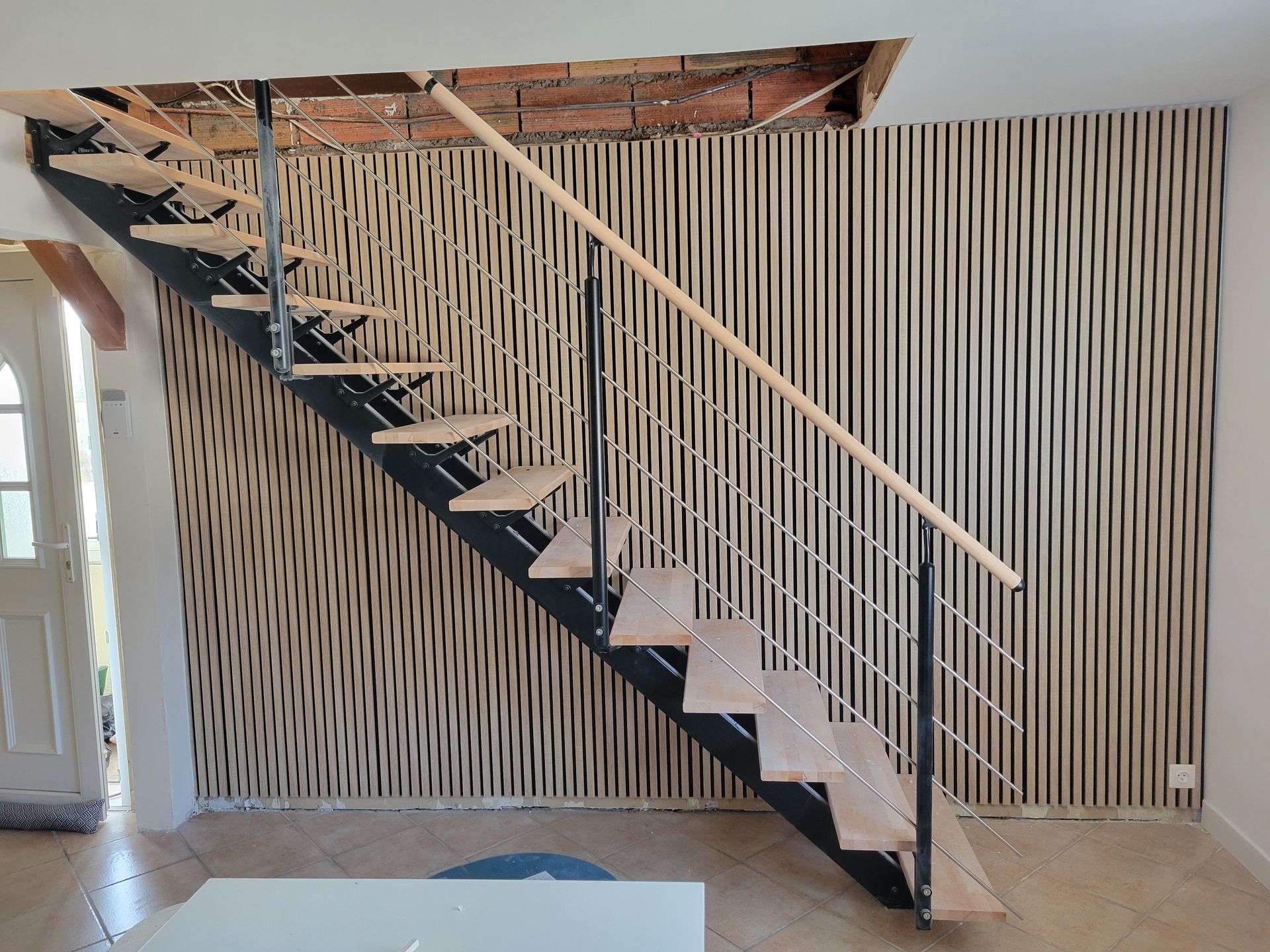 Escalier ouvert avec marches noires et rampes blanches contre un mur rayé dans un intérieur moderne