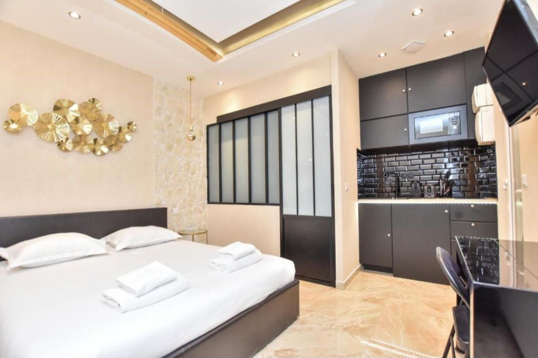 Chambre d'hôtel moderne avec lit, cloison coulissante en verre et kitchenette compacte aux tons neutres