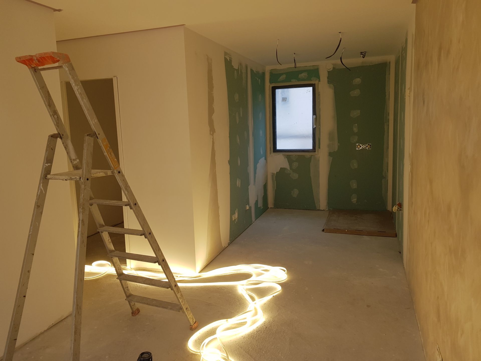 Pièce en rénovation avec échelle, murs bruts et lumière du soleil inondant le sol