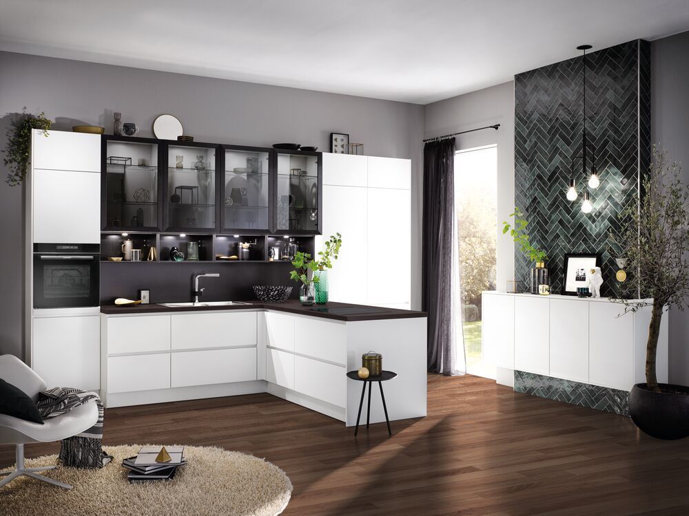 Eine Küche mit weißen Fronten und einer schwarzen Arbeitsplatte. Die Hochschränke haben Rauchglastüren.