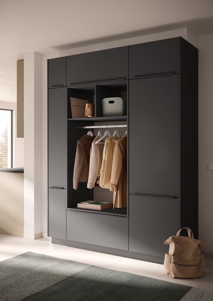 Ein schwarzer matter Kleiderschrank mit offener Mitte, darin hängt Kleidung in einem Flur.