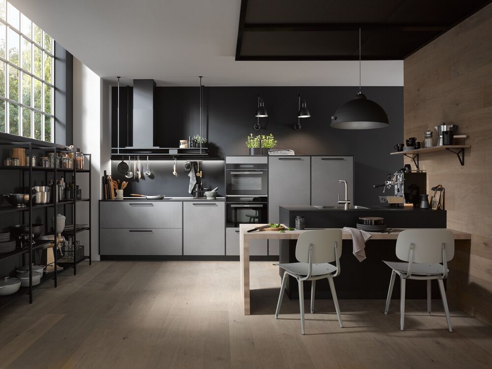 Eine dunkle Küche mit einer Zeile an der Wand und einer frei stehend im Raum. Die Fronten sind grau und schwarz.