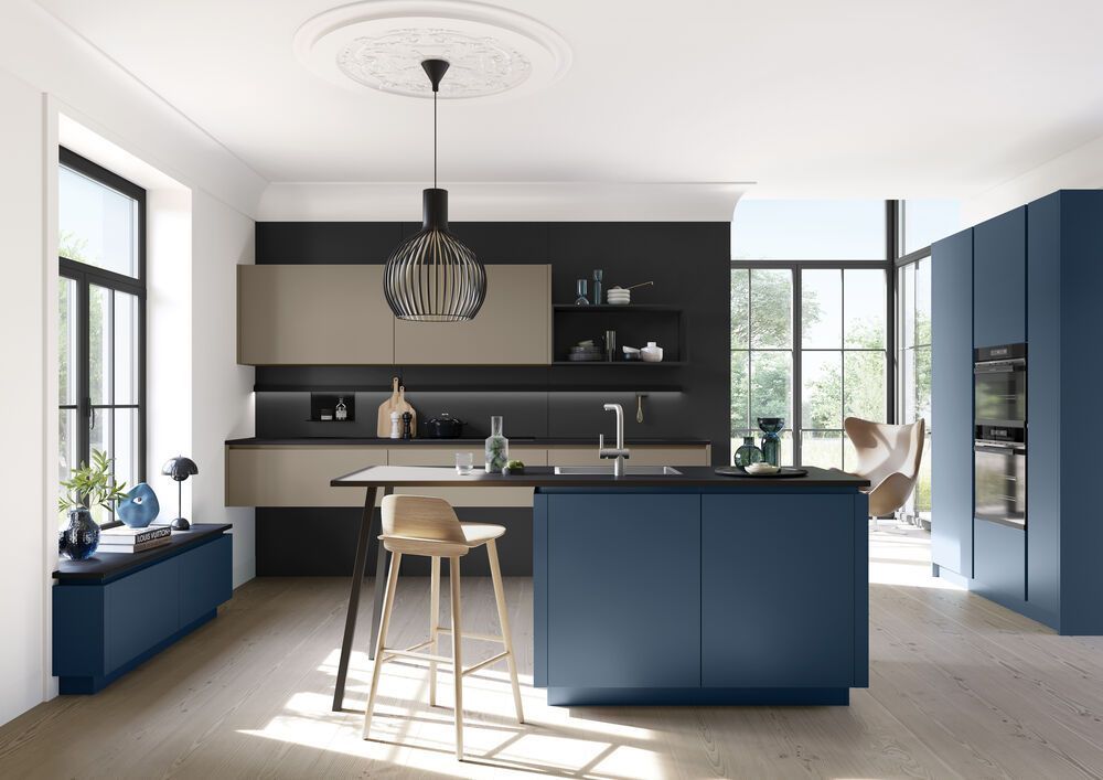 Eine Küche mit blauen und beigen Fronten. Zwei Küchenzeilen stehen jeweils an der Wand und eine Insel steht in der Mitte.