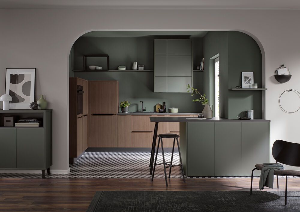 Eine Küche mit eleganten dunkelgrünen Schränken und Fronten im Holz-Look. Die Küche befindet sich in einer offenen Nische.