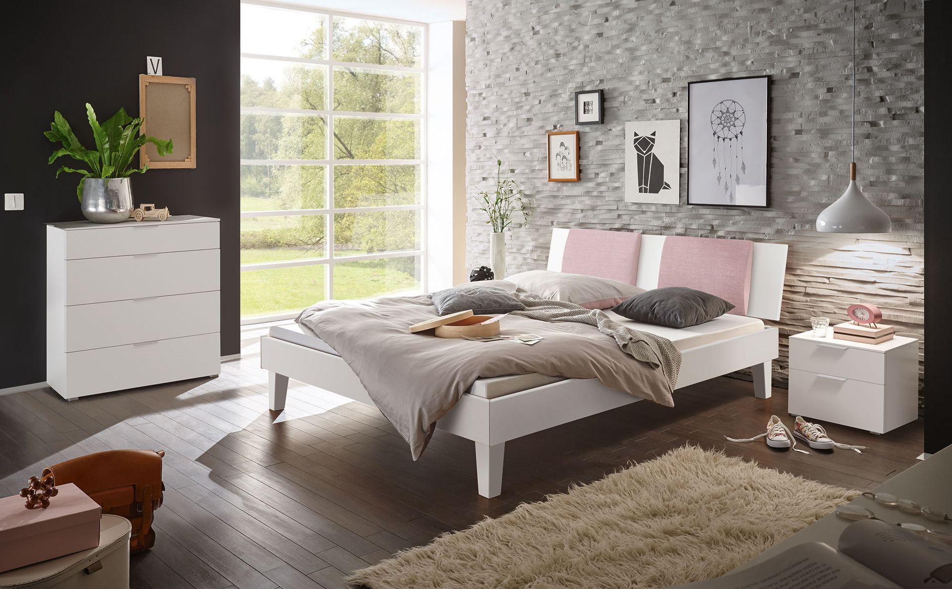 Schlafzimmer mit weißem Bett, Kommode und Nachttisch; graue Akzentwand, Fenster und Teppich.