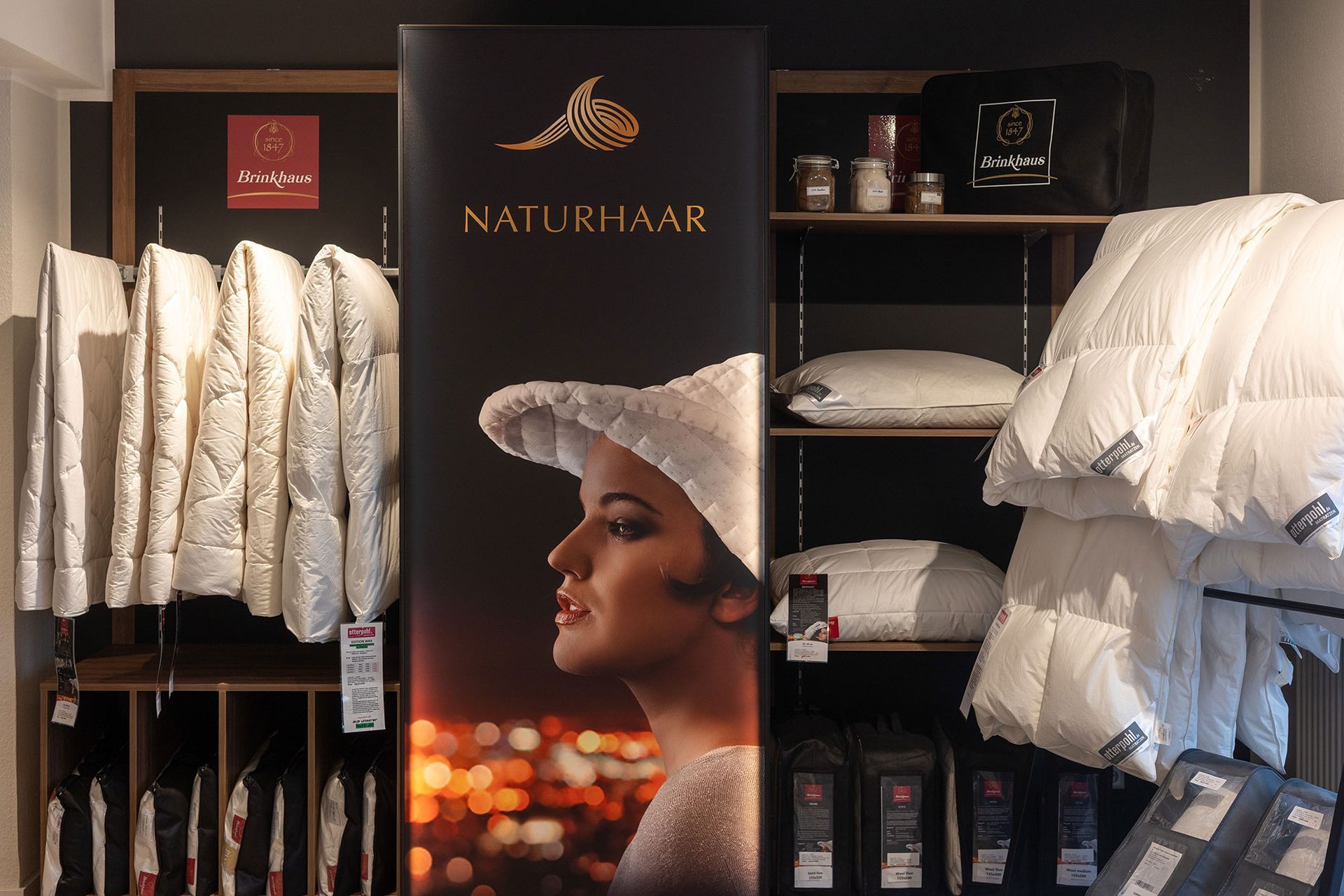 Schaufensterdekoration mit Bettwäsche, Kissen und einem Werbebanner mit dem Profil einer Frau.