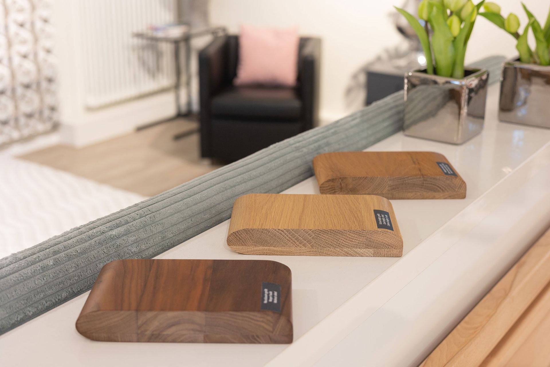 Holzproben auf weißem Untergrund, im verschwommenen Hintergrund sind ein Stuhl und Blumen zu sehen.