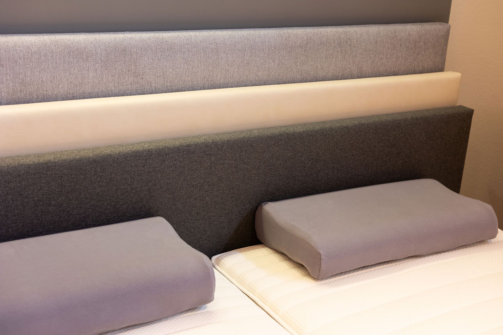 Ausgestellte Matratzenschichten und Kissen; verschiedene Grau- und Weißtöne.