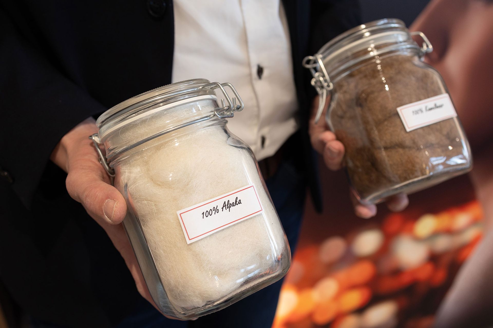 Zwei Glasgefäße mit Fasern: eines mit der Aufschrift „100% Alpaka“ und eines mit der Aufschrift „100% Leder“.
