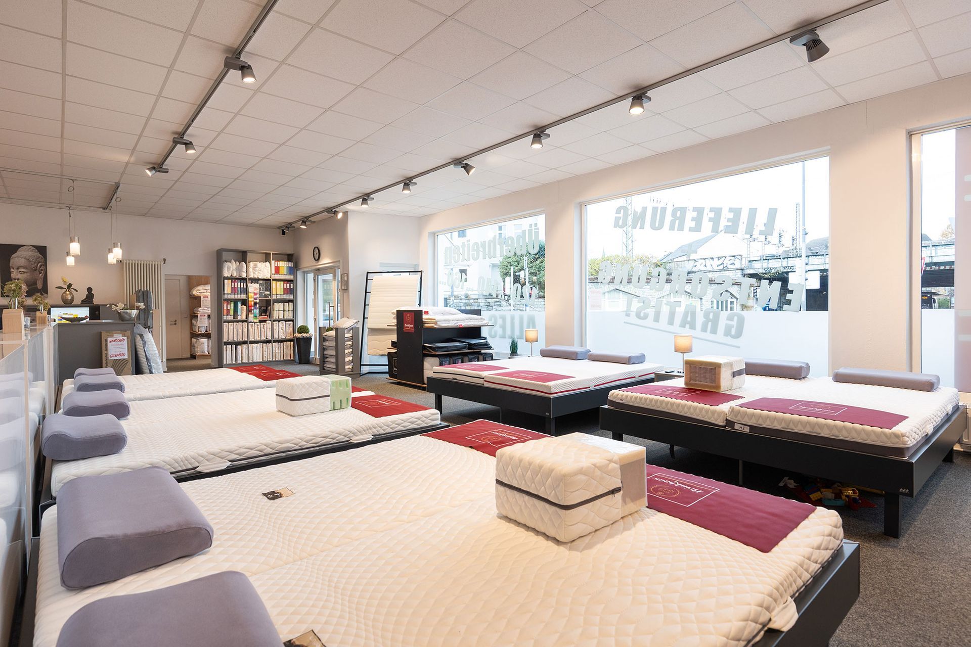 Innenansicht eines Matratzengeschäfts mit ausgestellten Betten, heller Beleuchtung und großen Fenstern.