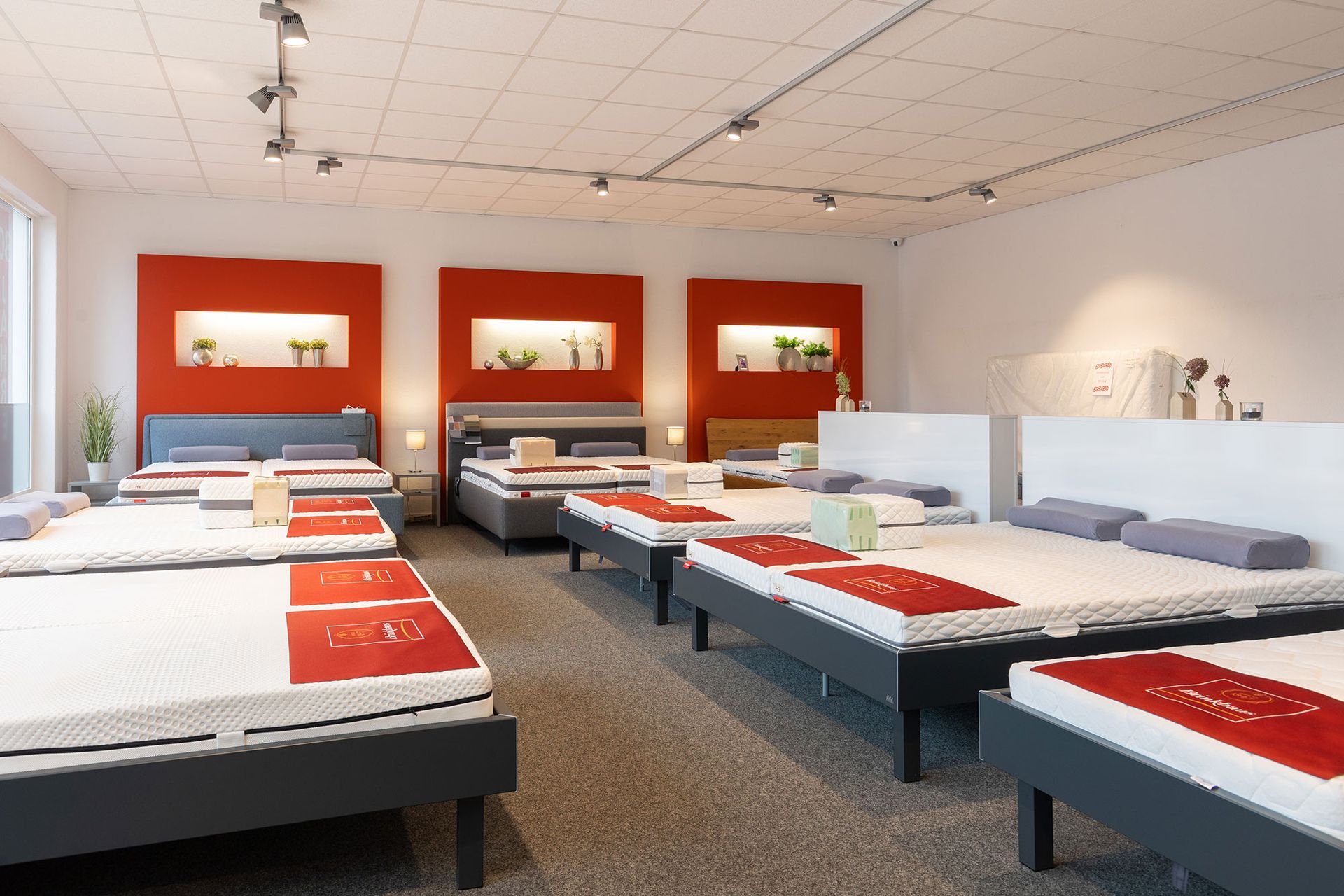 Innenansicht eines Matratzengeschäfts mit ausgestellten Betten und roten Akzenten.