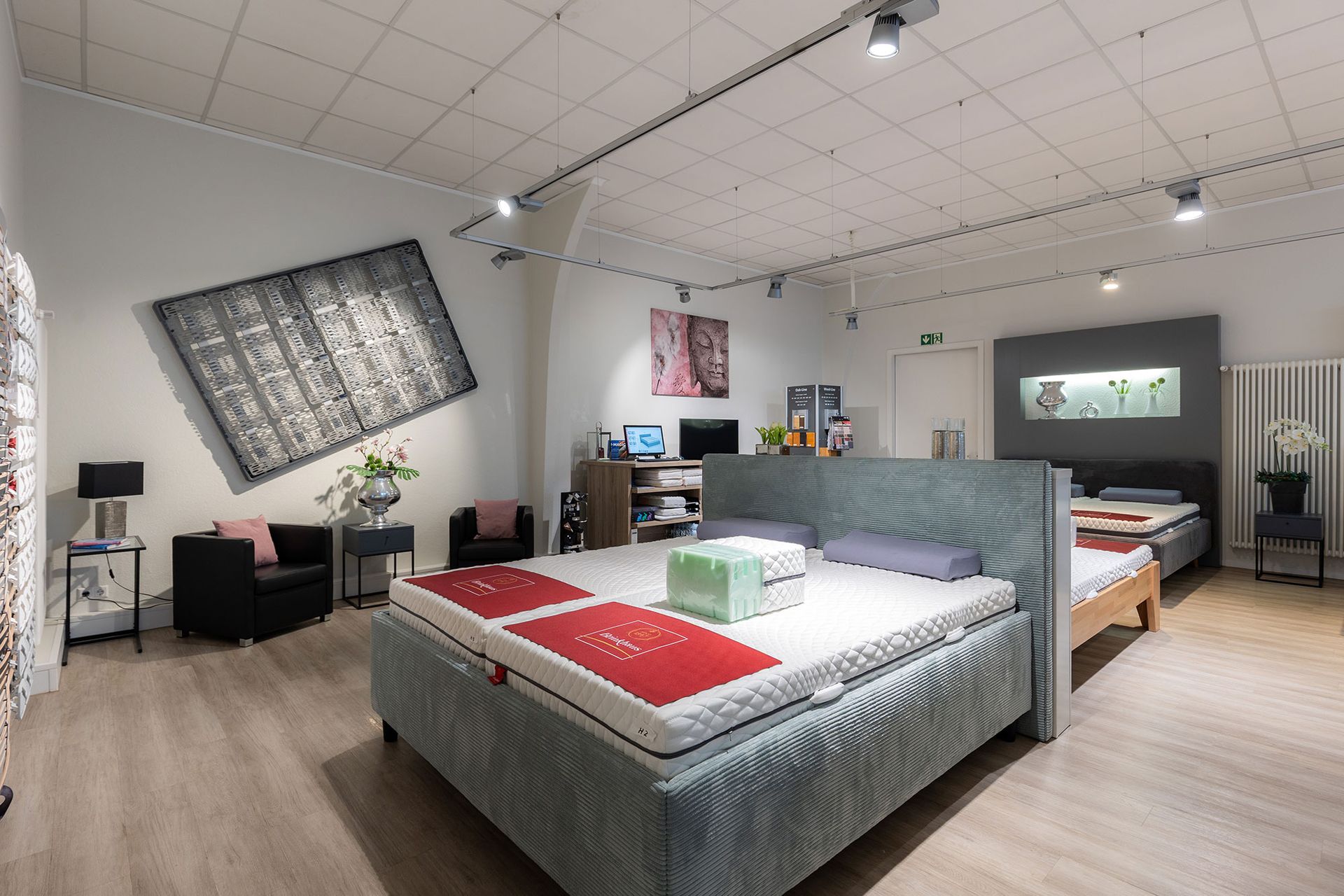 Innenansicht eines Matratzengeschäfts mit Betten, Kunstwerken und verschiedenen Beleuchtungselementen.