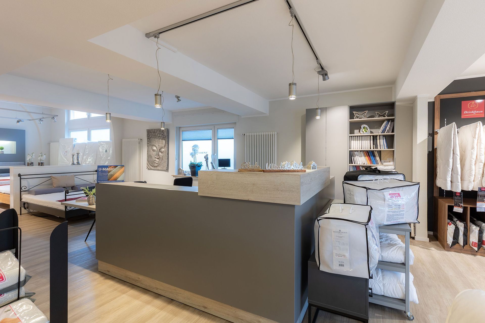 Innenansicht eines Ladens mit grauem Empfangstresen, Ausstellungsregalen, Bettwäsche und Schaufenster.