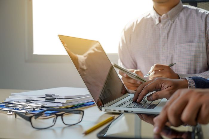 Personas trabajando en un escritorio con un portátil, papeles y gafas en una oficina luminosa