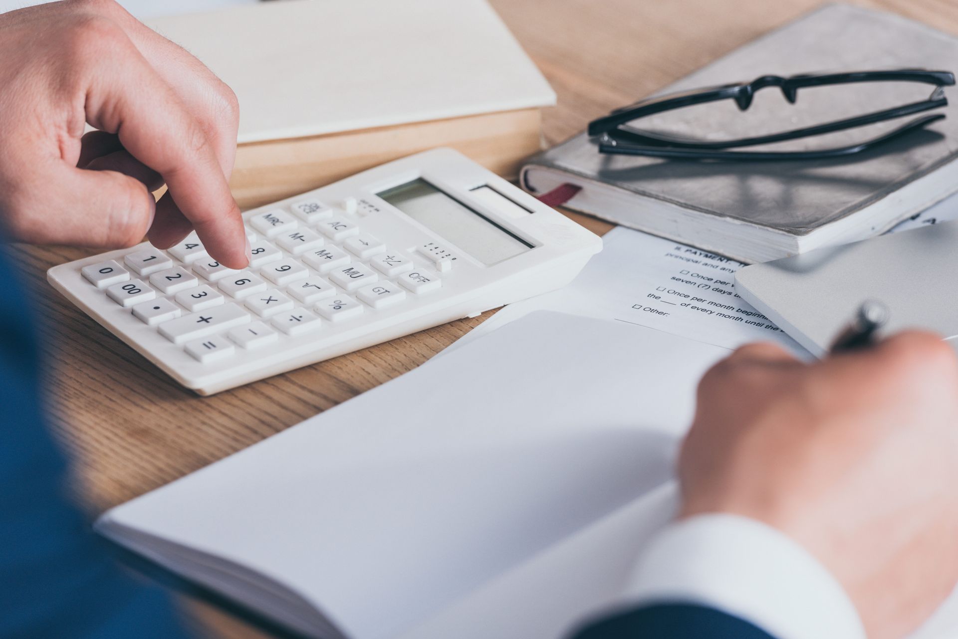 Manos usando una calculadora junto a documentos y unas gafas sobre un escritorio