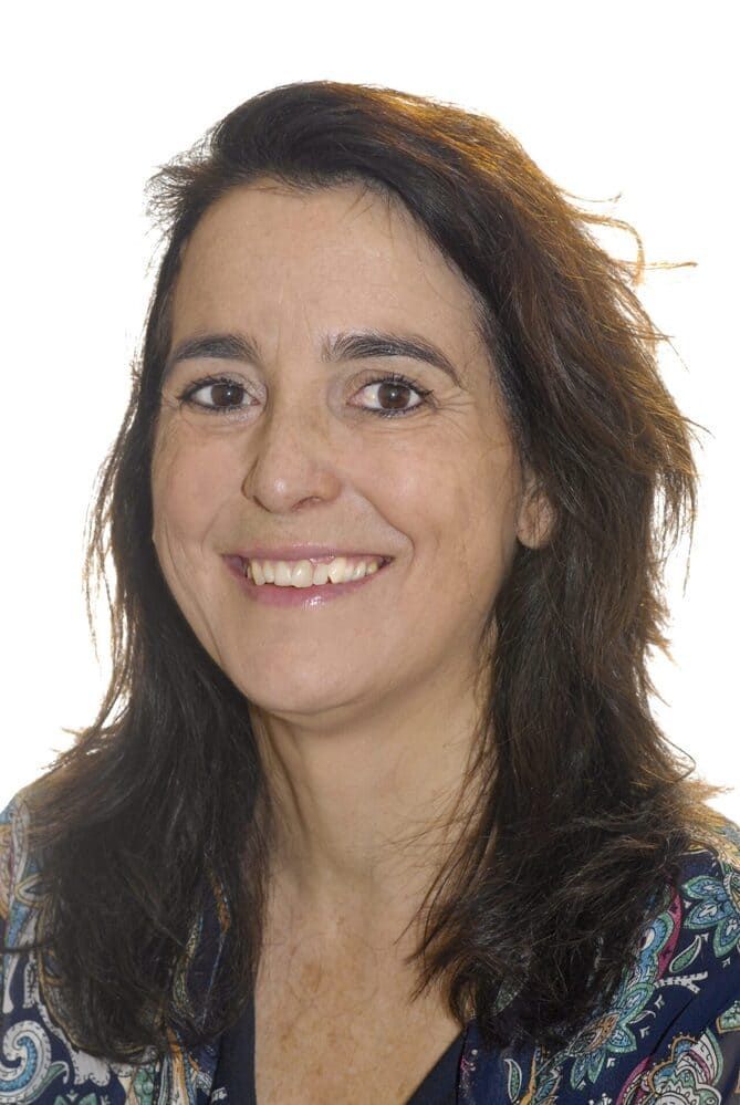 Mujer sonriente de cabello oscuro y blusa estampada sobre un fondo blanco