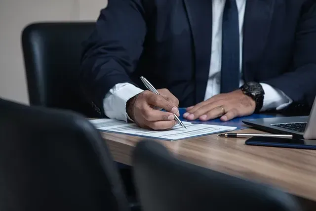 Persona de traje escribiendo en un escritorio con un bolígrafo.