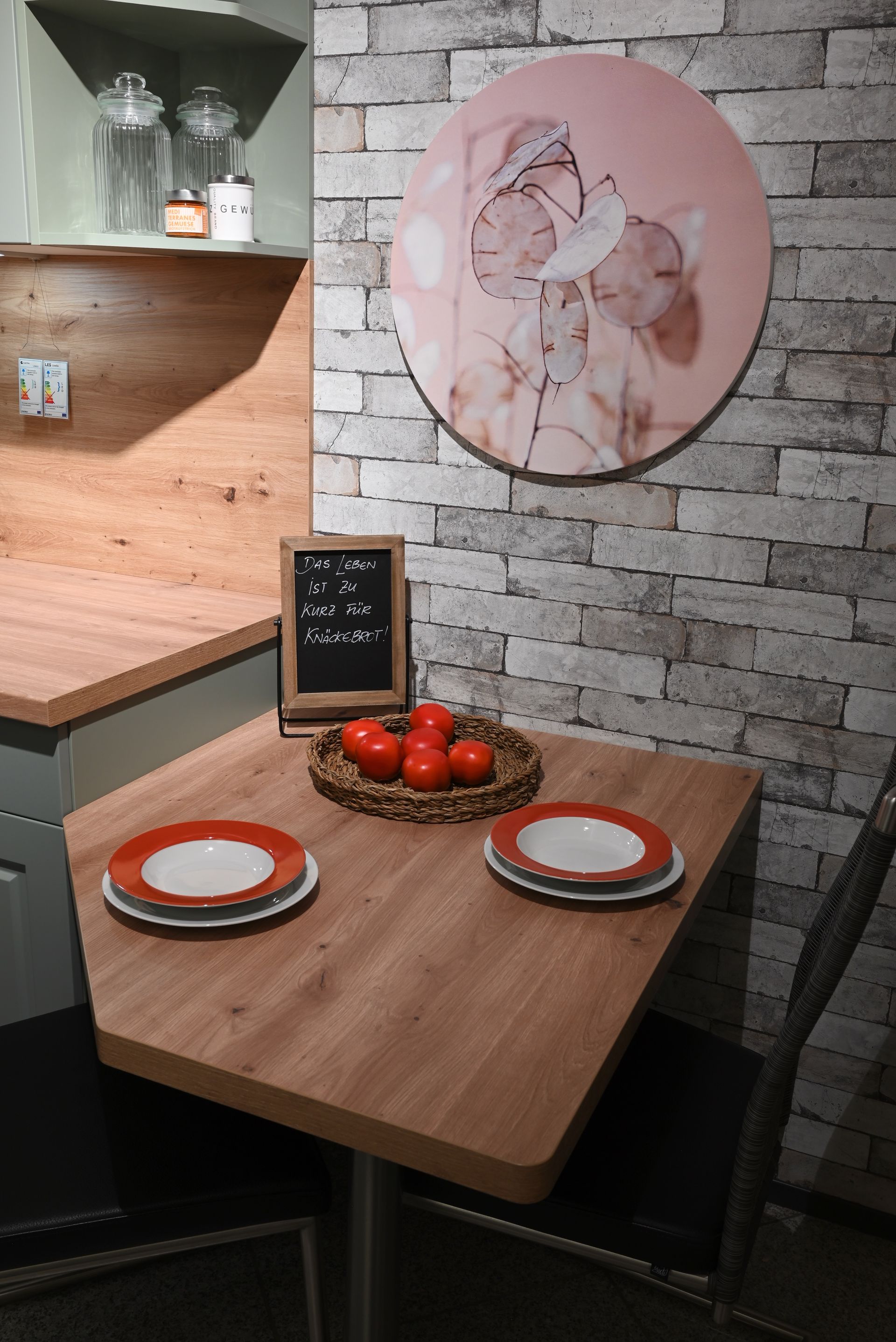 Ein kleiner Holztisch mit Tellern und Tomaten darauf in einer Küche.