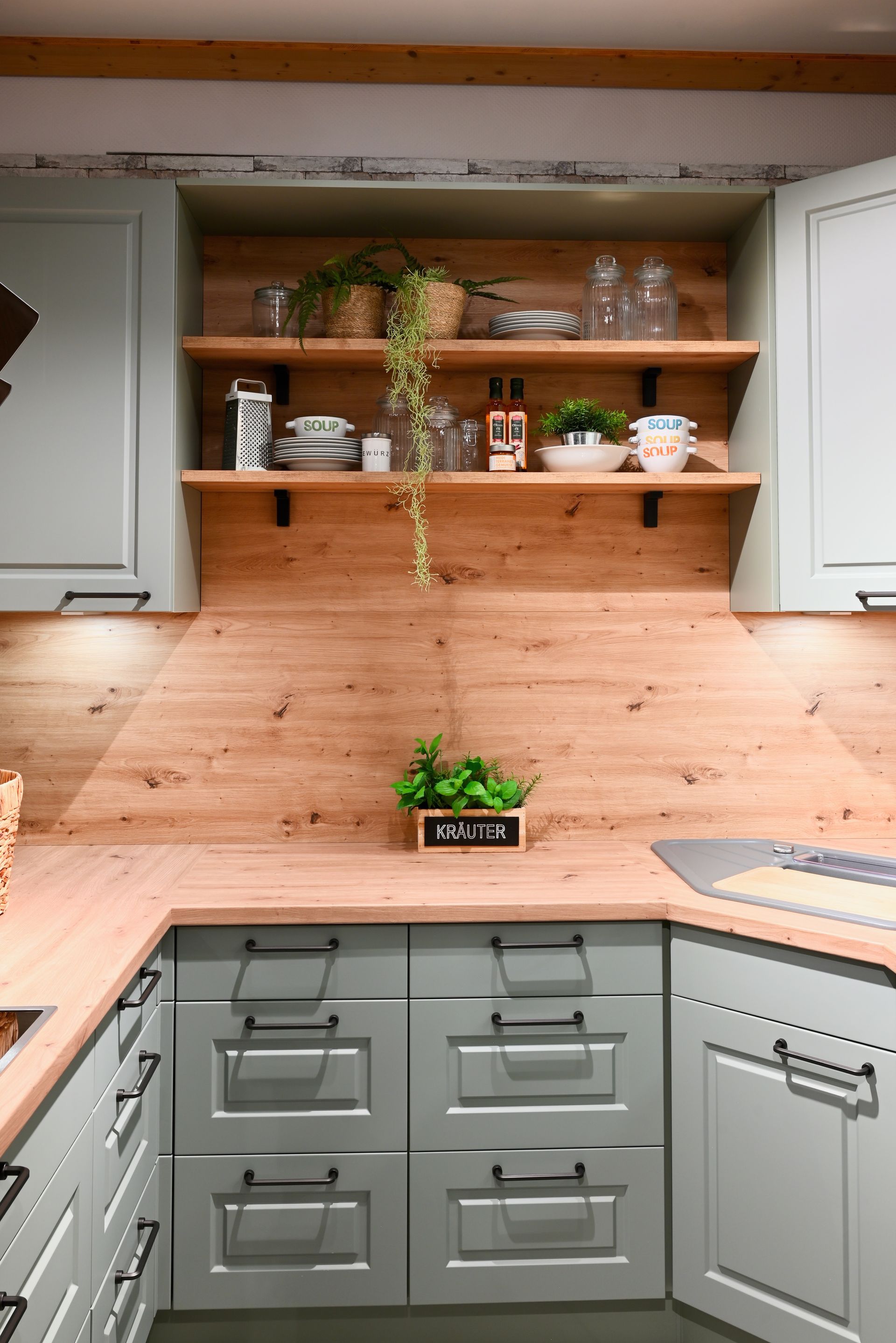 Eine Küche mit grauen Schränken und Holzregalen.