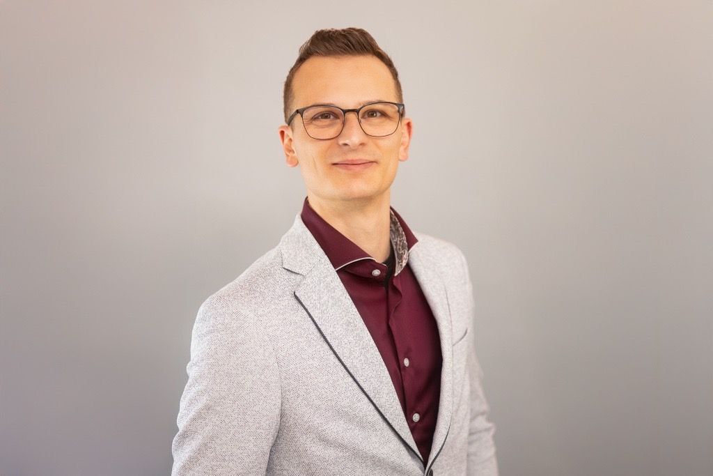 Ein junger Mann mit Brille und schwarzem Hemd lächelt in die Kamera.