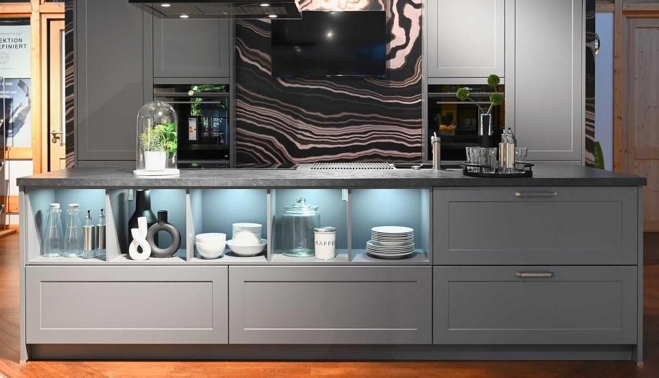 Eine Küche mit grauen Schränken und einer schwarzen Arbeitsplatte