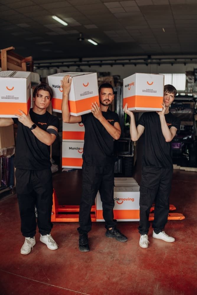 Mujer empacando una caja, colocando plástico de burbujas alrededor de un artículo decorativo, hombre empacando en el fondo.