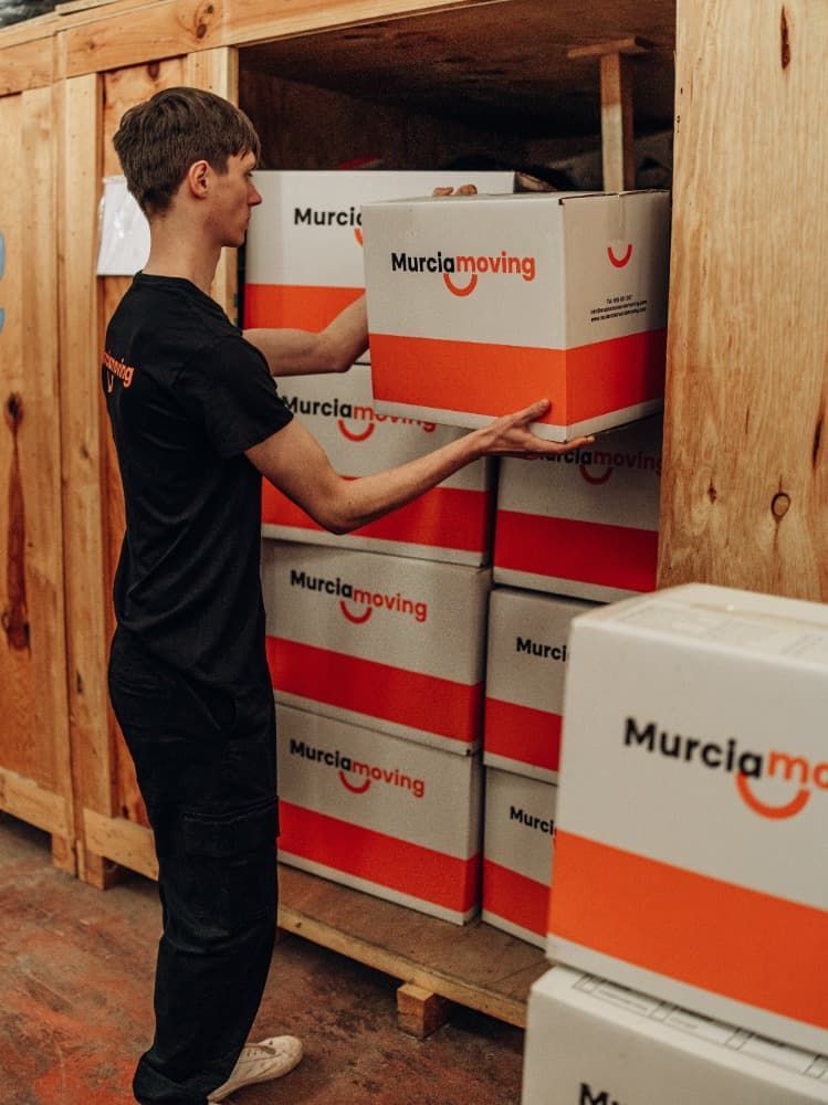 Mujer empacando una caja, colocando plástico de burbujas alrededor de un artículo decorativo, hombre empacando en el fondo.