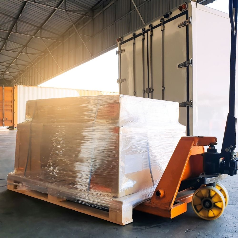 Mujer empacando una caja, colocando plástico de burbujas alrededor de un artículo decorativo, hombre empacando en el fondo.