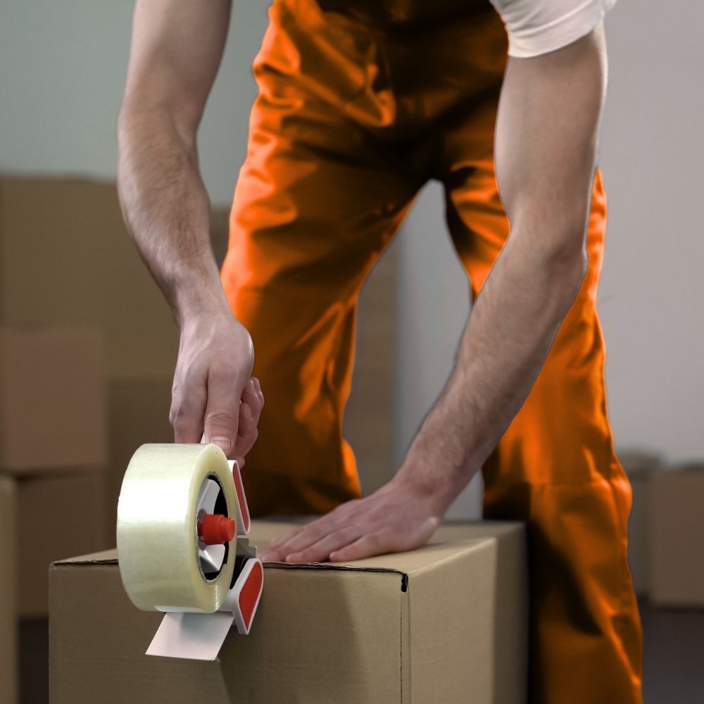 Mujer empacando una caja, colocando plástico de burbujas alrededor de un artículo decorativo, hombre empacando en el fondo.