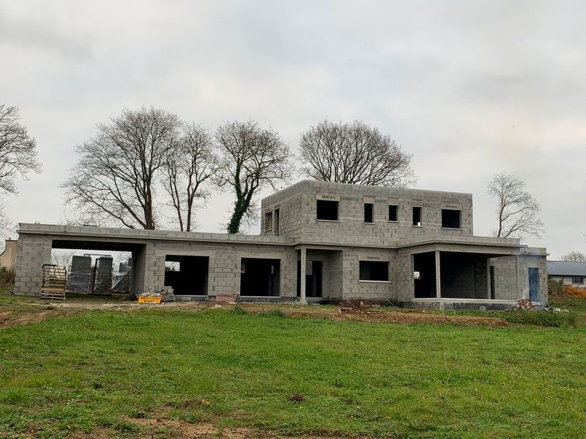 Maison en briques partiellement construite, avec structure de garage apparente et matériaux de construction à l'extérieur.