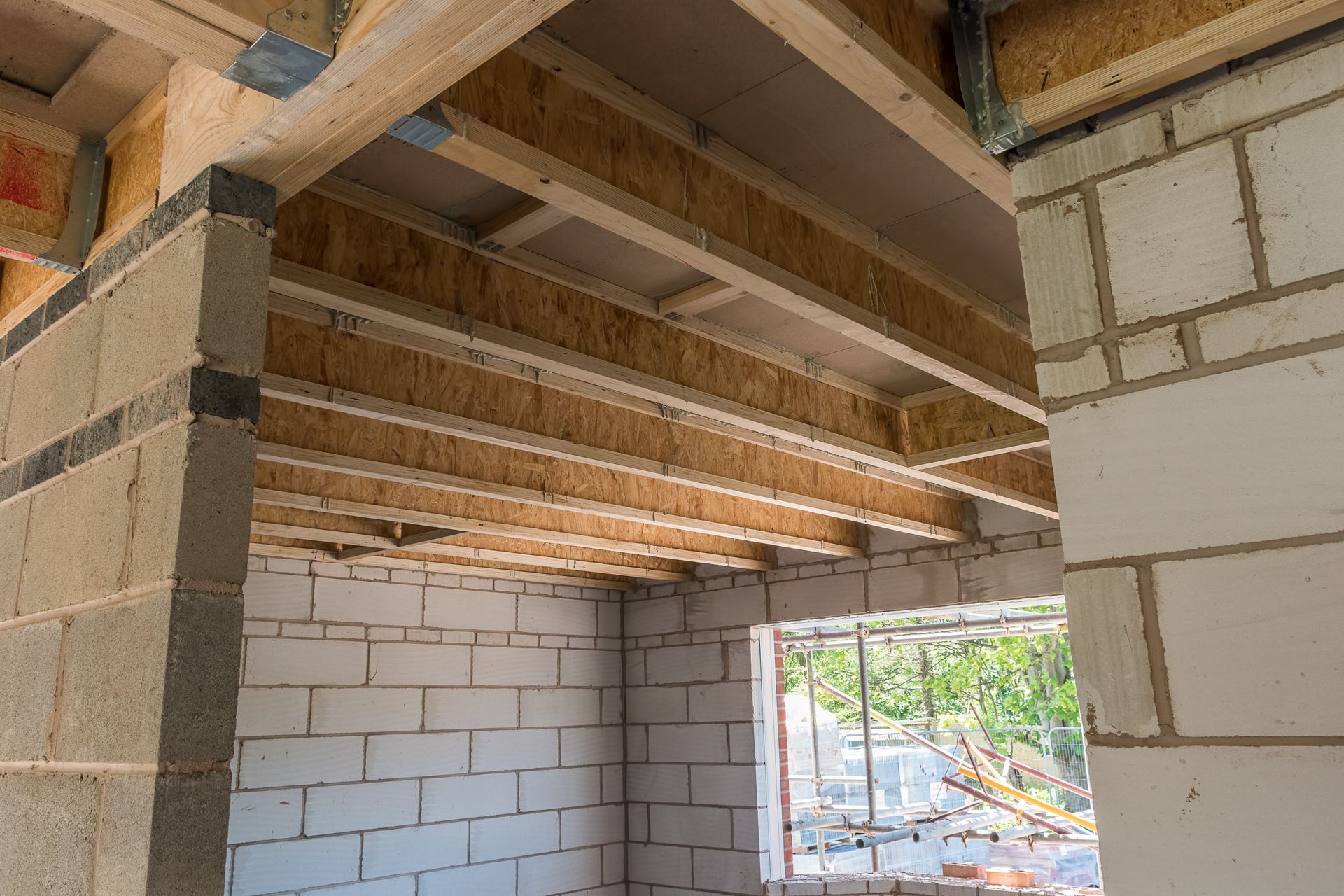 Intérieur d'un chantier de construction avec murs en parpaings blancs, poutres en bois apparentes et charpente de plafond.
