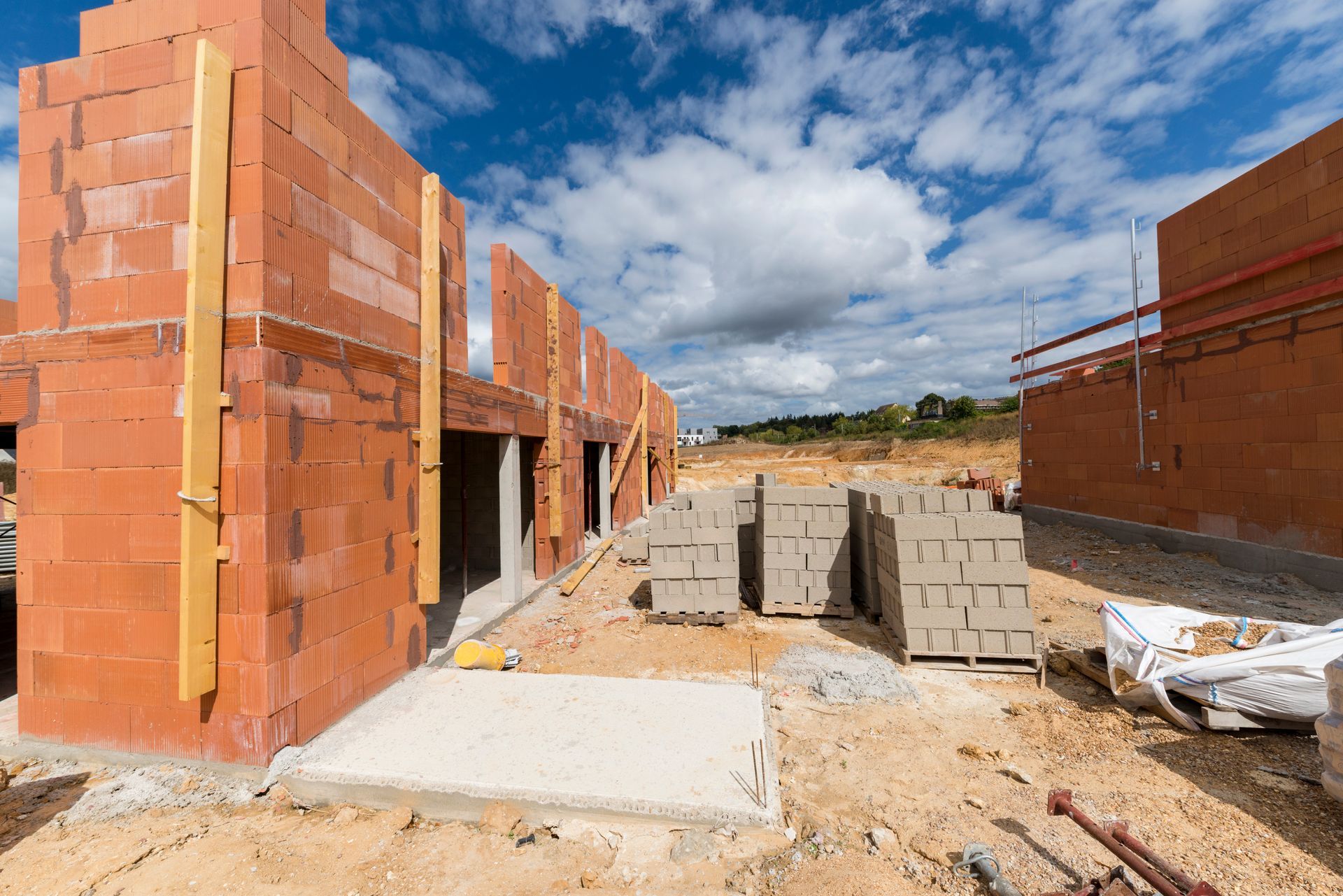 Chantier de construction avec des murs de briques inachevés et des blocs de béton empilés.