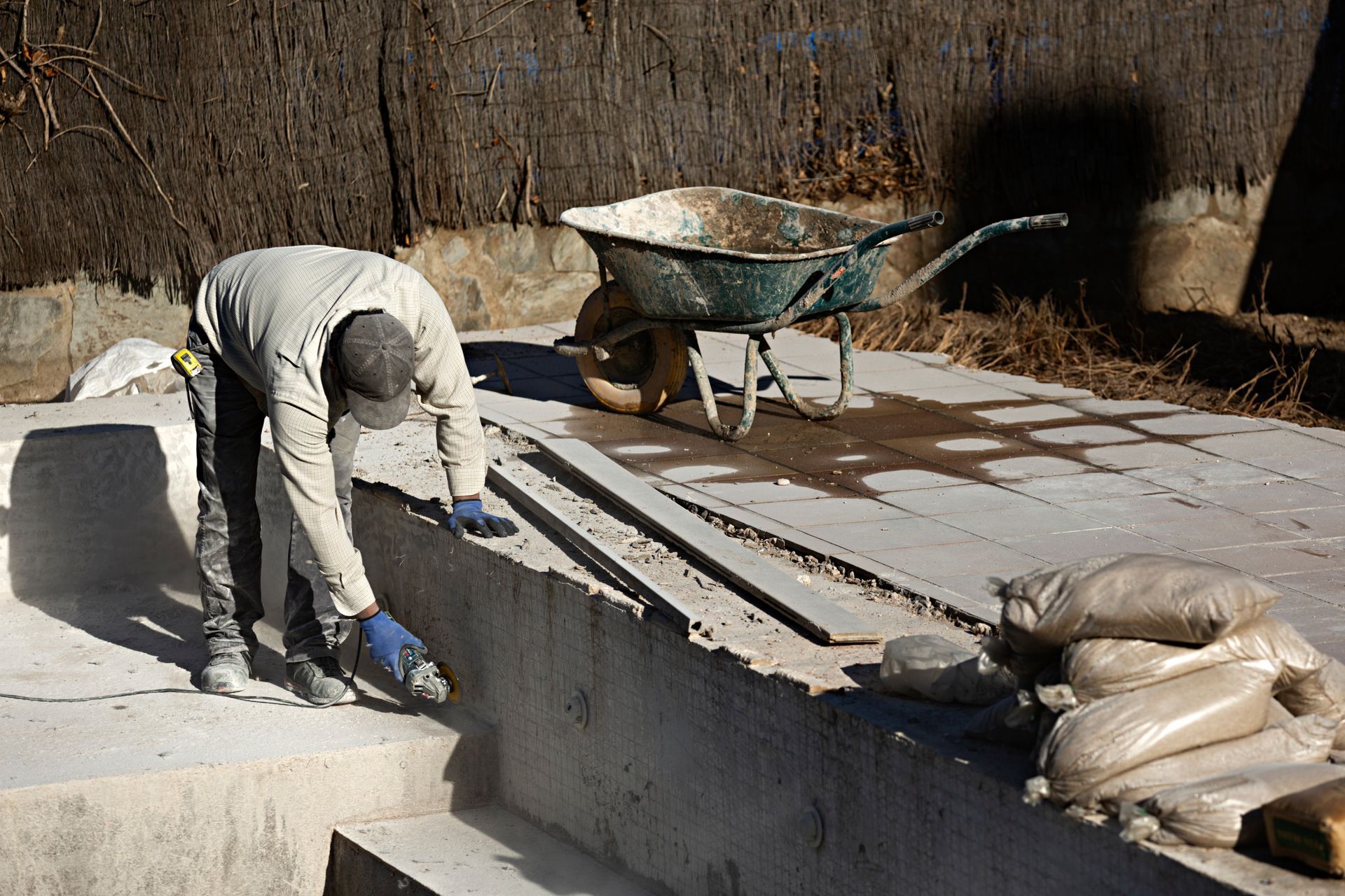Un ouvrier lisse du béton frais à côté d'une brouette et de sacs sur un chantier.