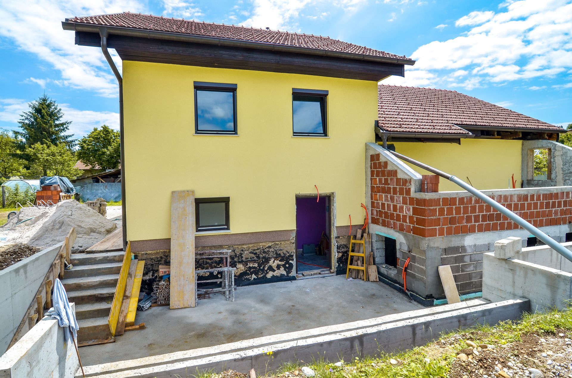 Maison jaune de deux étages en construction, avec échafaudages et maçonnerie en façade.